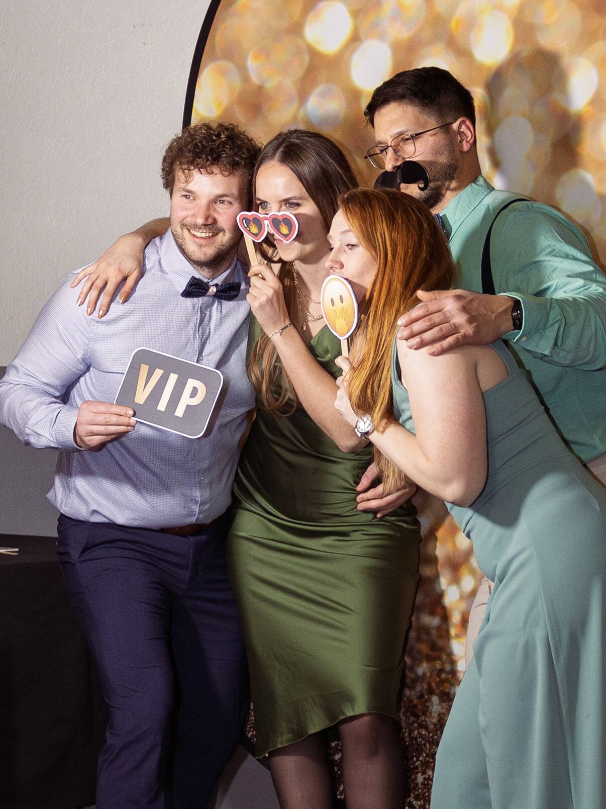 Groupe de personnes souriantes tenant des accessoires festifs devant un photobooth lors d’un événement.